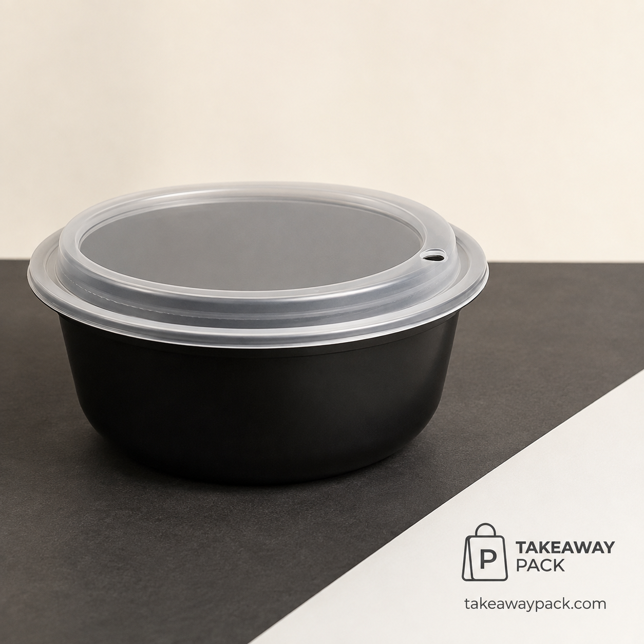 Black round food bowl with a clear vented lid on a black-and-white surface
