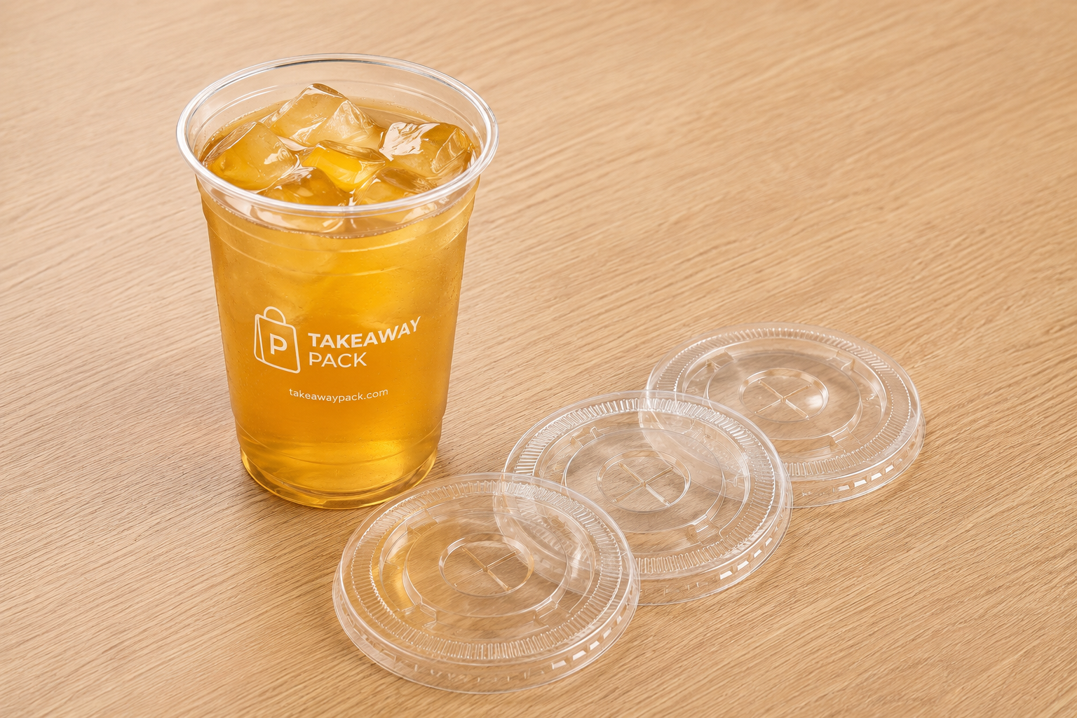 Clear PET cold cup with iced drink beside three flat lids on a wood surface